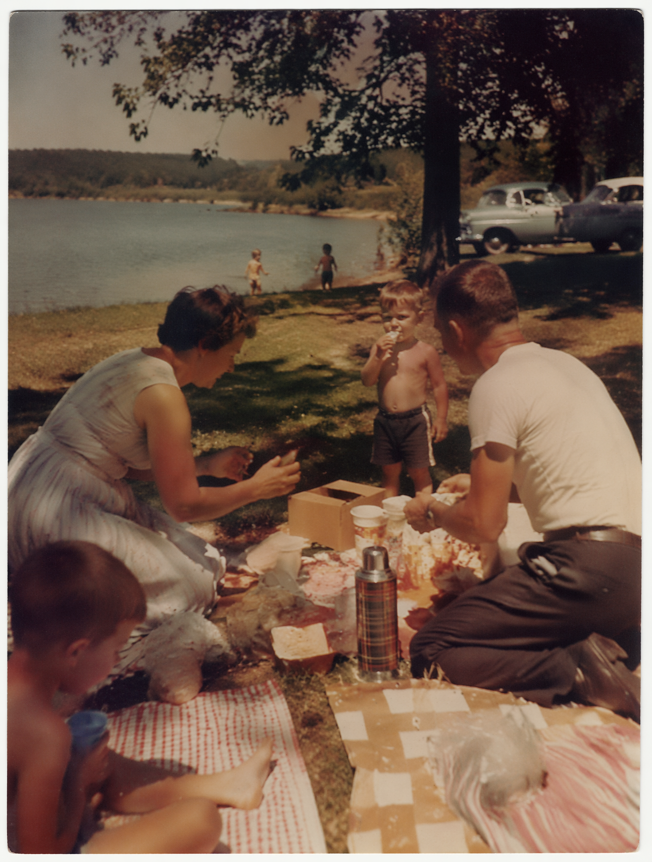 1950s family picnic beside a peaceful lake, adults preparing