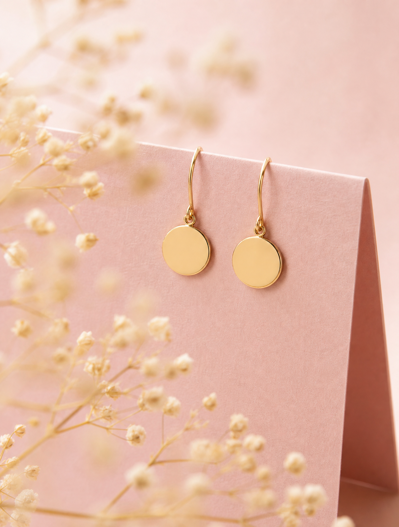 A pair of minimalist gold disc earrings hang delicately from