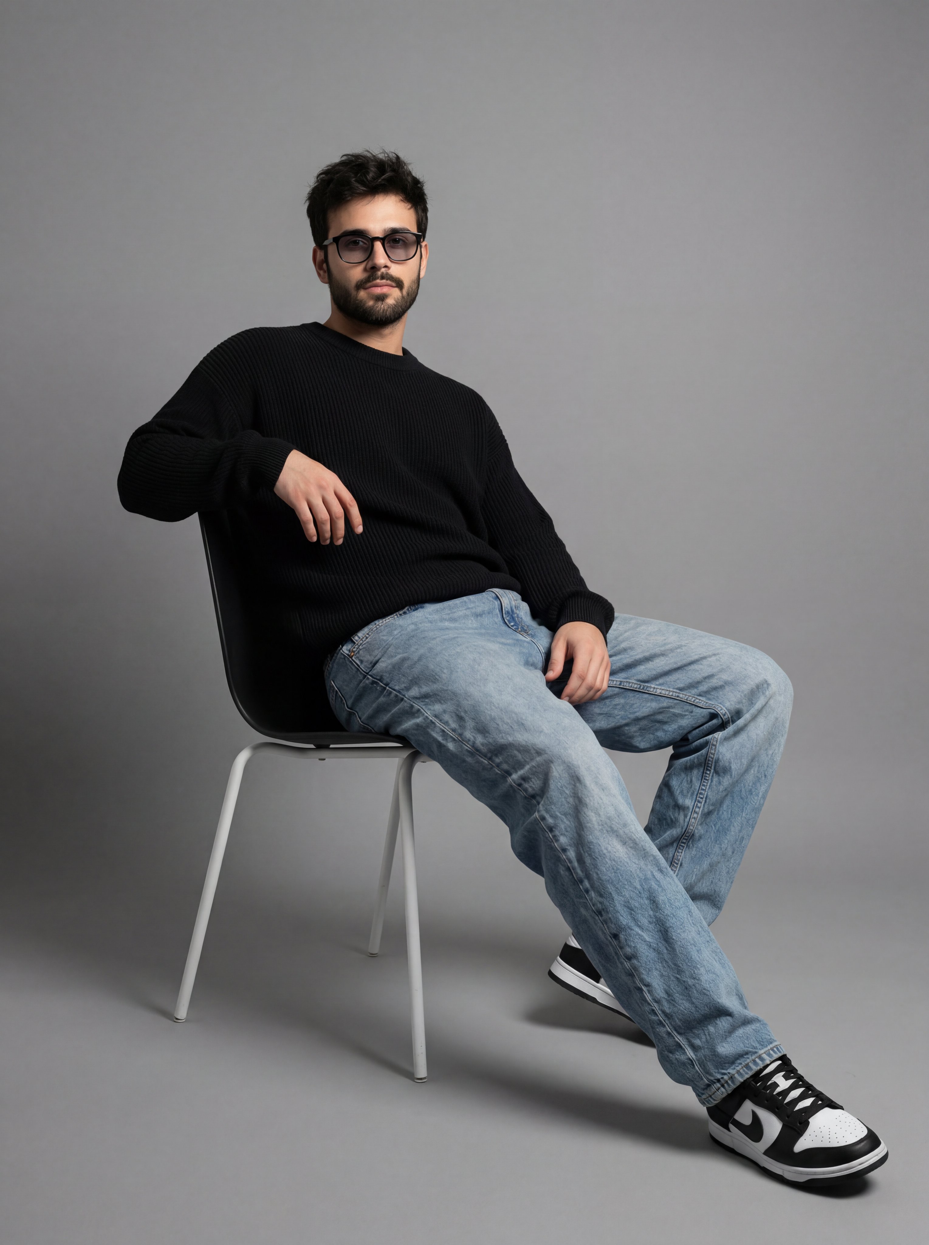 A full-length studio portrait of a young man with dark, mess