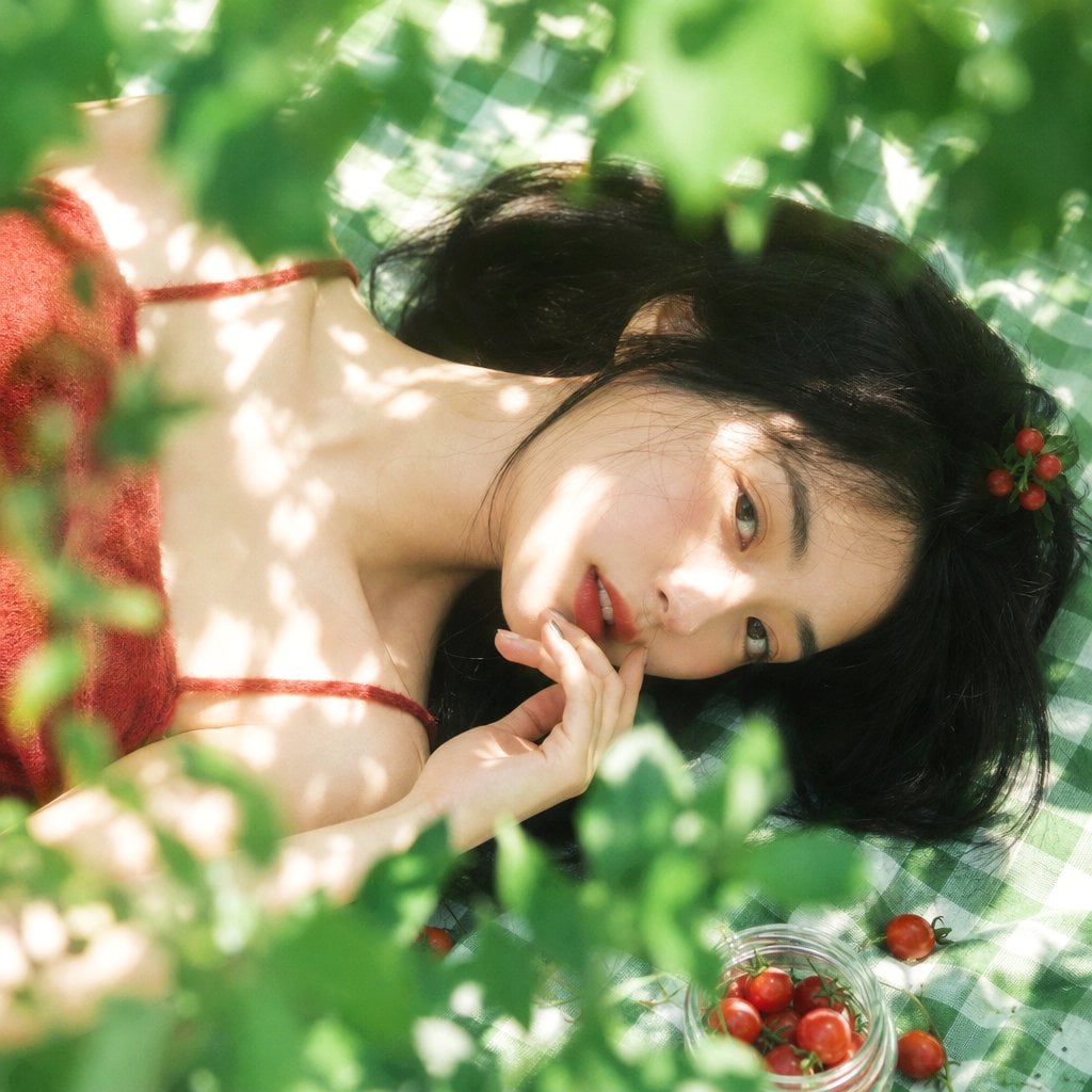 真人摄影,夏日植物系生活方式写真,清透日系胶片感,竖幅 2:3,俯拍近景到面部特写,年轻女性横向躺在绿白格纹野餐布上,脸