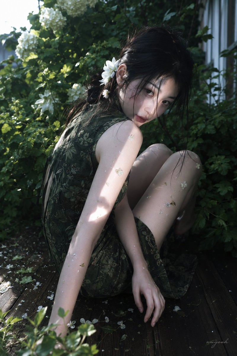真人摄影，真实人物，户外花园唯美人像写真，低饱和冷绿调与斑驳自然光，轻微胶片柔焦和电影感。竖幅近中景，略高机位俯拍，人物